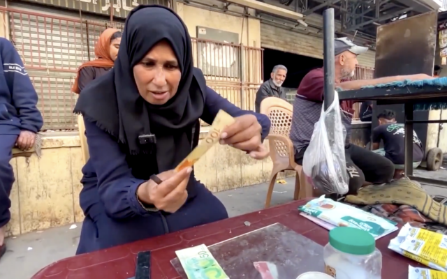 Une femme de Gaza brandit un billet de 100 NIS (31 dollars), affirmant qu'il a perdu environ 20 % de sa valeur en raison de l'usure due à la guerre, dans une vidéo publiée par Reuters le 31 octobre 2025. (Capture d'écran : X/Reuters)